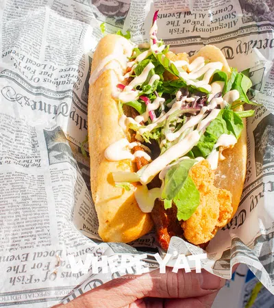 Fresh fried fish sandwich with lettuce and sauce served in newspaper-style wrapping held by a person.