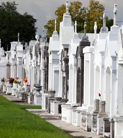 Row of white and gray above-ground tombs with flowers in a cemetery on a sunny day.