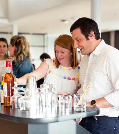 People enjoying drinks and socializing around a modern bar counter with bottles and glasses.