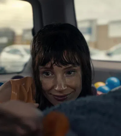 Woman with wet hair smiling inside a car filled with colorful plastic balls, looking at someone out of focus.
