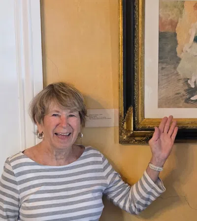 Smiling elderly woman pointing at framed impressionist painting of ballerina in museum setting