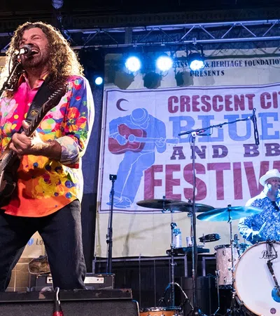 Singer with colorful shirt plays guitar and vocalist performs at Crescent City Blues and BBQ Festival concert.