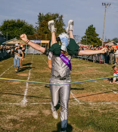 Person in eagle costume winning a race while carrying another runner across the finish line at outdoor event.