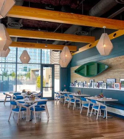 Bright modern restaurant interior with wooden beams, blue walls, hanging lights, and framed photos on a bench.