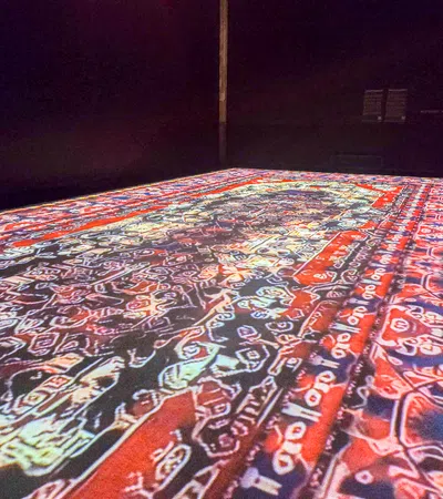 Colorful abstract patterned carpet with red, blue, and white geometric designs laid out on floor in dark room.