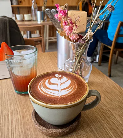 Cup of latte art coffee with iced drink garnished with strawberry and dried flowers on cafe table