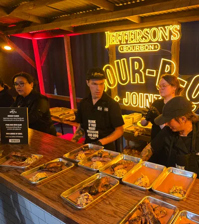 Food stall serving barbecue with brisket and ribs under bright Jefferson's Bourbon neon sign at event