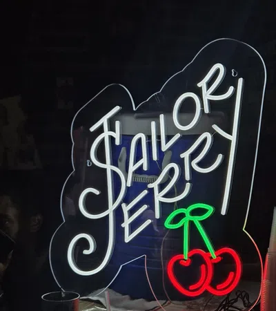 Neon sign displaying the words Sailor Jerry with bright white and red cherry graphics on a dark background.