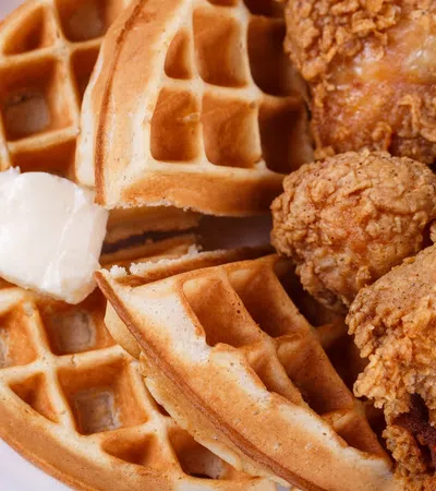 Crispy fried chicken pieces served with golden waffles and a dollop of melting butter on a white plate.
