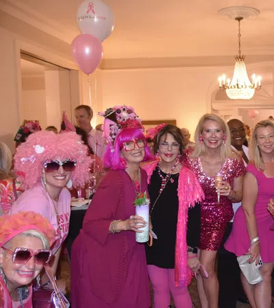 Group of women dressed in pink and black at an indoor party with balloons and drinks celebrating together.