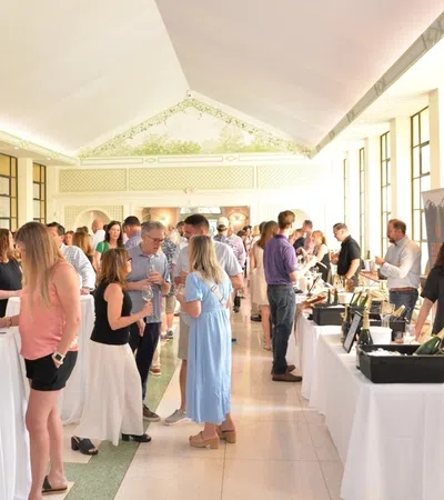 Guests mingle and sample wines at an indoor tasting event with bright natural light and elegant decor