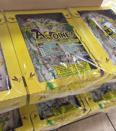 Stacked boxes of Antoine's King Cake with yellow packaging, showcasing traditional Mardi Gras colors and design.