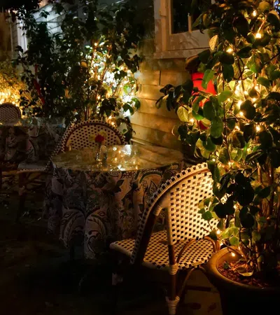 Cozy outdoor cafe seating with patterned chairs and tables lit by warm string lights at night.