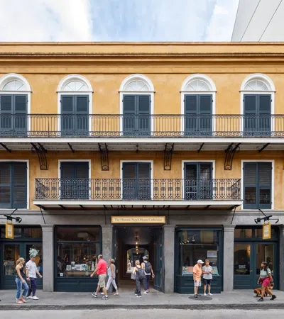 Historic yellow building with black shutters and iron balconies in a lively urban street scene.