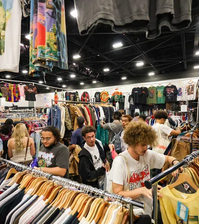 Young shoppers browsing vintage and graphic t-shirts on racks at a busy indoor clothing market.