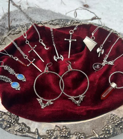 Silver fantasy pendants including swords, crescent moon, dragon, and gemstone jewelry on red velvet in silver tray