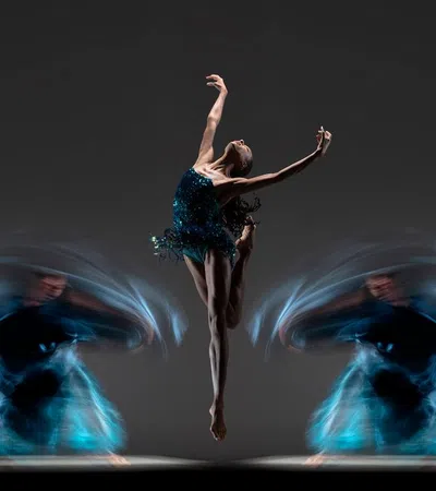 Ballet dancer in mid-air leap with blurred motion trails of dancers spinning on either side against dark background