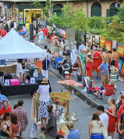 Outdoor art market with crowds browsing vibrant paintings displayed along a street on a sunny day