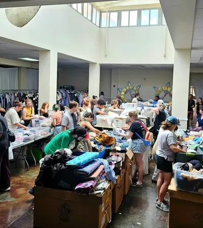 Volunteers sorting and organizing clothing donations in a large, well-lit community center with boxes and racks of clothes.