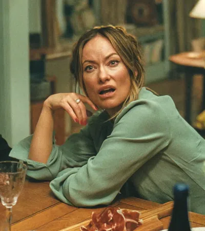 Two women with serious expressions sitting at a wooden table in a cozy, warmly lit room.