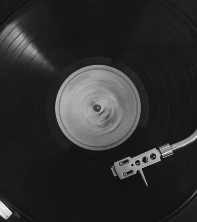 Black vinyl record spinning on a turntable with a silver tonearm in black and white photo.