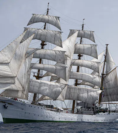 Large white sailing ship with multiple sails and a Colombian flag on the ocean under clear sky