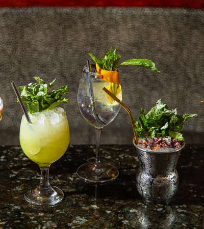 Five colorful cocktails with garnishes like mint, citrus, and berries on a dark granite bar counter.