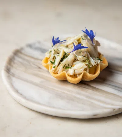 Gourmet tartlet filled with crab meat and garnished with blue edible flowers on a marble plate.