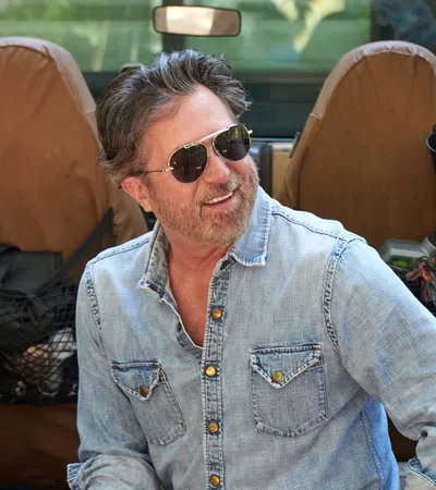Man wearing sunglasses and denim shirt sitting in an open Jeep with tan seats smiling outdoors