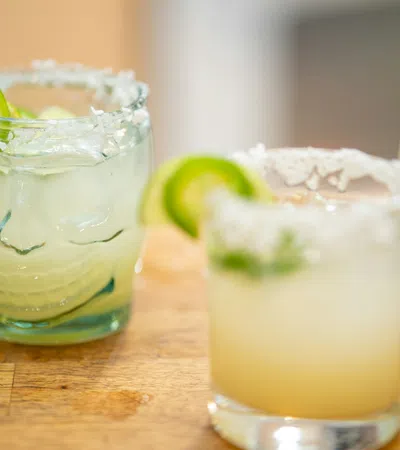 Three margarita cocktails with salted rims and lime garnish on a wooden surface.