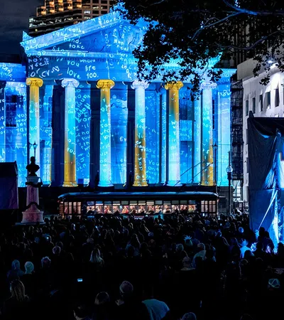 Crowd at night watching blue and gold light projections on a classical building during Luna Fête festival.