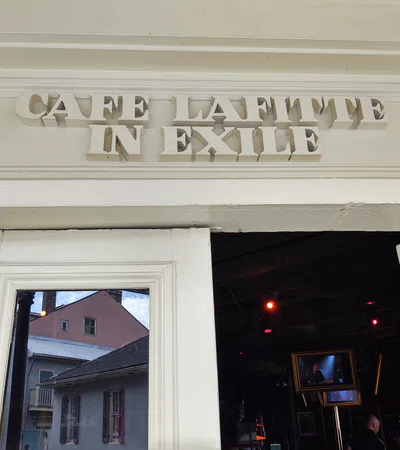 Entrance of Cafe Lafitte in Exile with white wooden doors and reflective glass showing buildings outside.