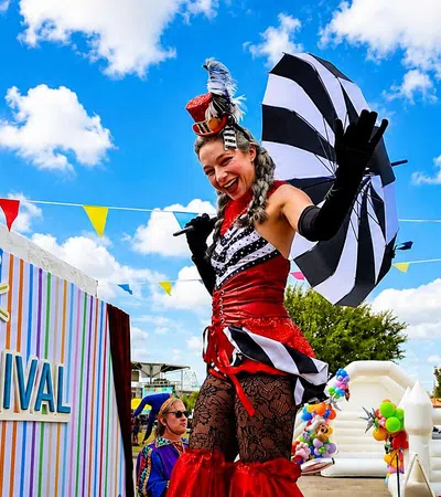 Performers in colorful carnival costumes entertain at LASPCA's outdoor community carnival event under a bright blue sky.