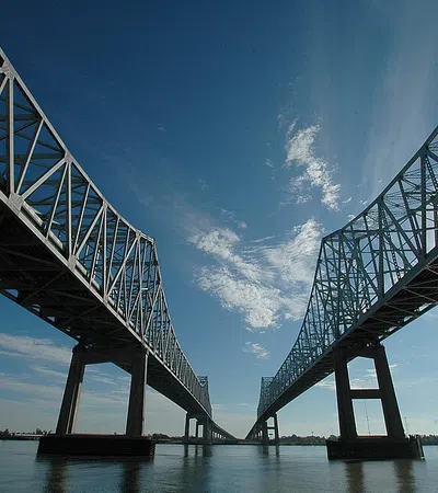 Steel truss bridge over calm river under blue sky with scattered white clouds on a sunny day