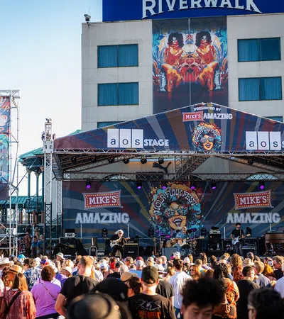 Outdoor music festival on Mike's Amazing stage at Riverwalk with large crowd enjoying live band performance.