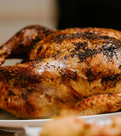 Golden-brown roasted whole chicken with herbs on a white plate ready to serve.