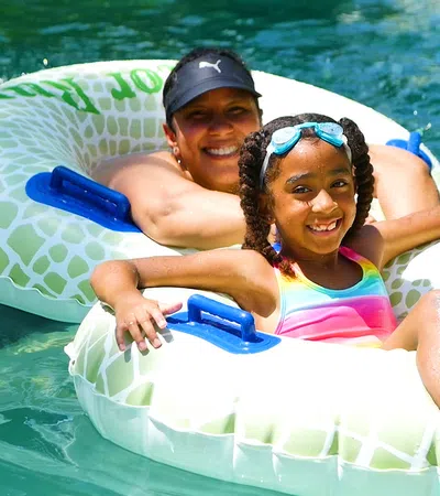 Smiling woman and girl in colorful swimsuit enjoying a sunny day on inflatable tubes in clear water.