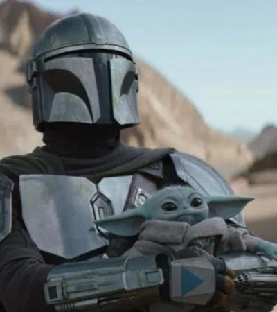 Armored Mandalorian holding Baby Yoda in desert landscape with rocky cliffs in background under clear sky