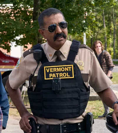 Vermont patrol officer in uniform speaking with a casually dressed man outdoors near an emergency vehicle.