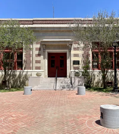 Brick building with red doors and windows, flanked by trees and black street lamps under a clear blue sky.