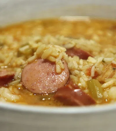 Close-up of a bowl of sausage and rice gumbo with vegetables in a savory broth.