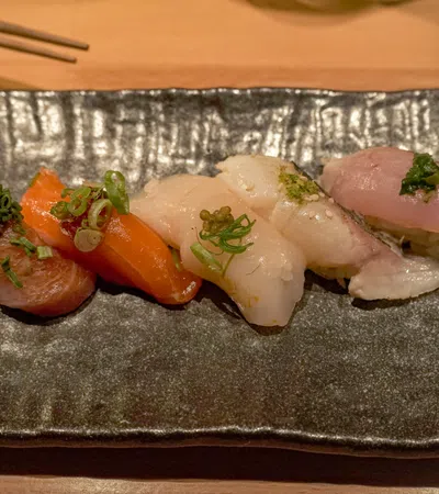 Assorted nigiri sushi with salmon, tuna, scallop, and white fish served on a black rectangular plate.