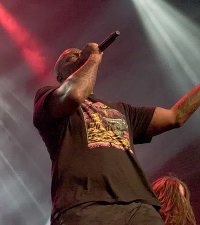 Male rapper performing passionately on stage with microphone amid dynamic stage lighting effects.