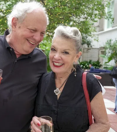 Happy elderly couple enjoying drinks at an outdoor social gathering on a sunny day.