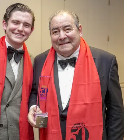 Two men in formal wear with red scarves, one holding a Best Chef award at an event.