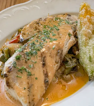 Grilled fish fillet topped with herb sauce served with fried zucchini flower on a white plate