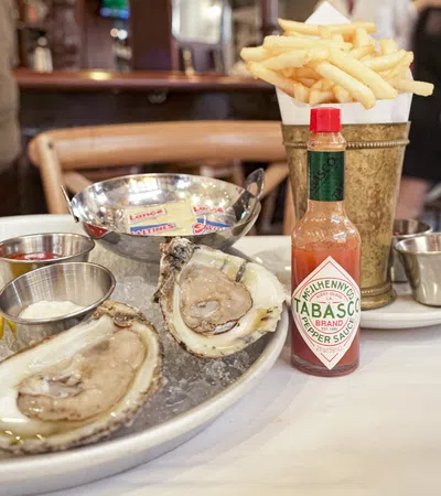 Fresh oysters on ice with fries and Tabasco sauce bottle served on a table in a restaurant.