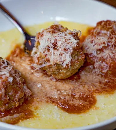 Three meatballs topped with grated cheese served in marinara sauce on a white plate.