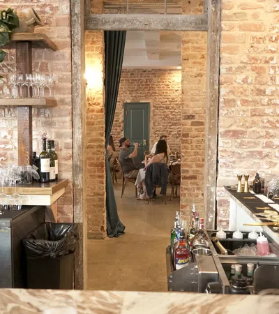 Interior view of a rustic bar and dining area with exposed brick walls and patrons seated at tables.