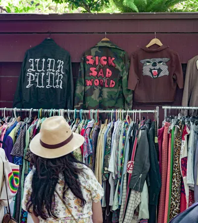 Two women browsing colorful clothes and jackets at an outdoor vintage clothing market stall.